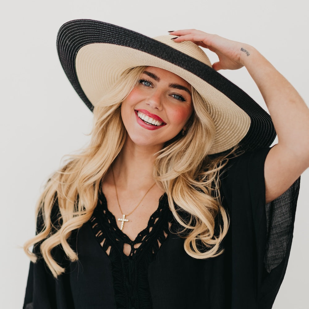 Two-tone wide floppy sun hat, black crown with tan brim and gold chain band, hand on brim