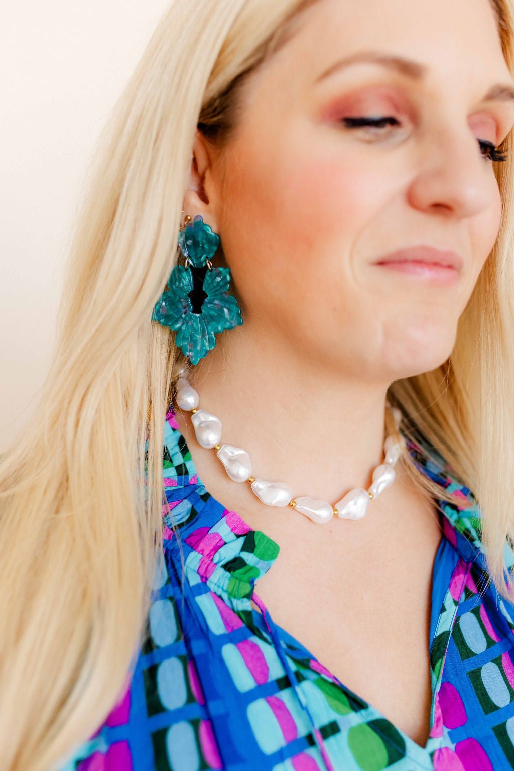 Turquoise floral statement earrings with layered petals, worn with colorful dress