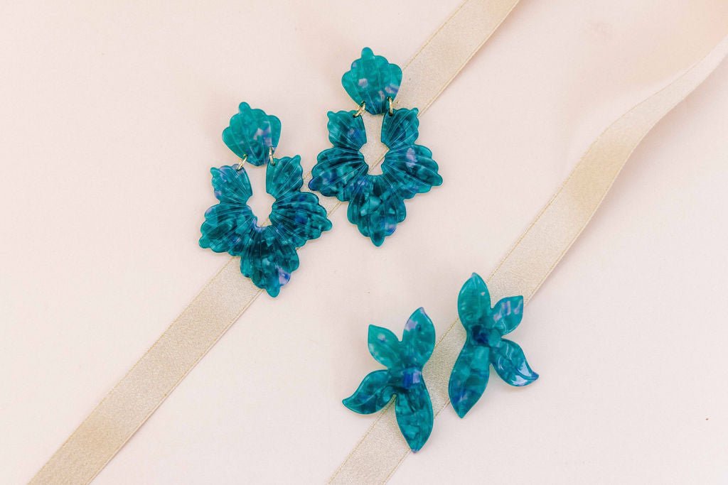Turquoise floral statement earrings laid flat on beige ribbon background