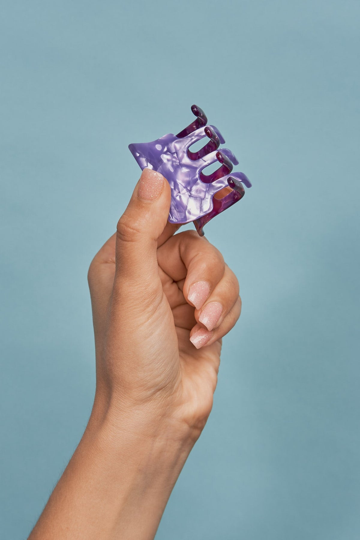 Purple mini hair claw clip held in a hand, multi-prong design