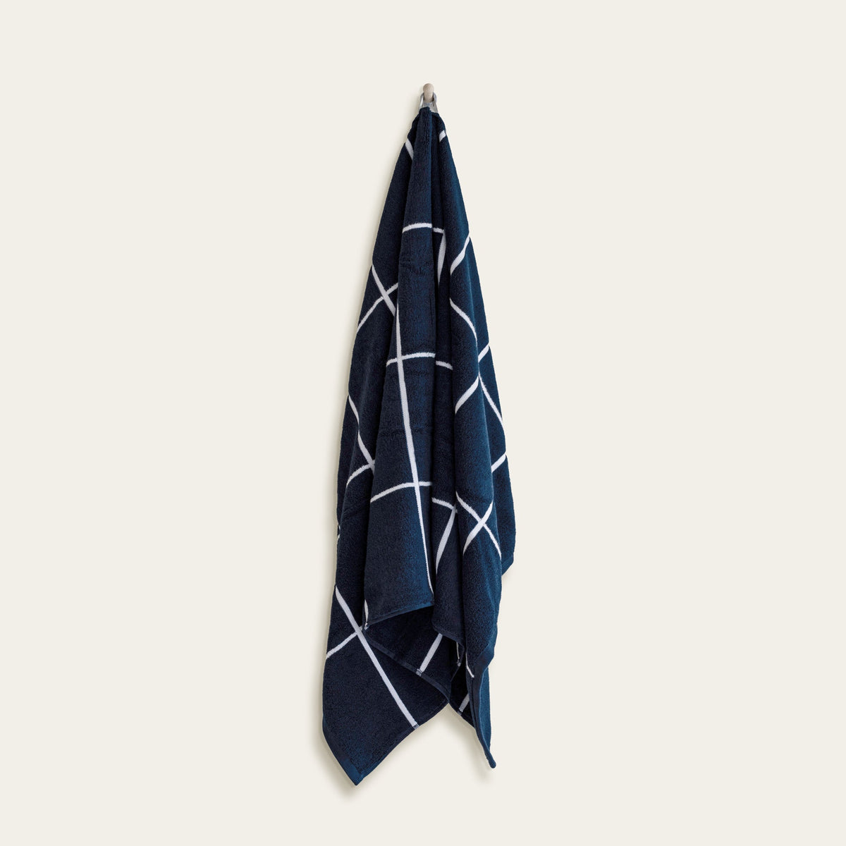 Navy cotton towel with white crosshatch lines, folded and hanging from a loop.