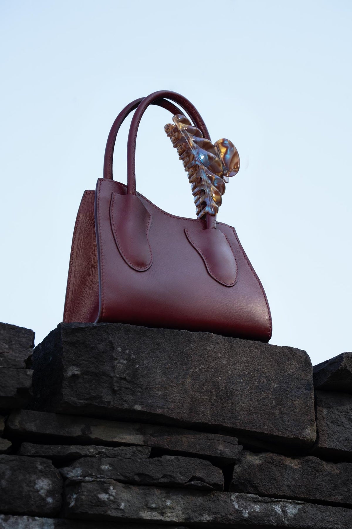 Croissant hair claw with marbled stones resting on burgundy handbag handle