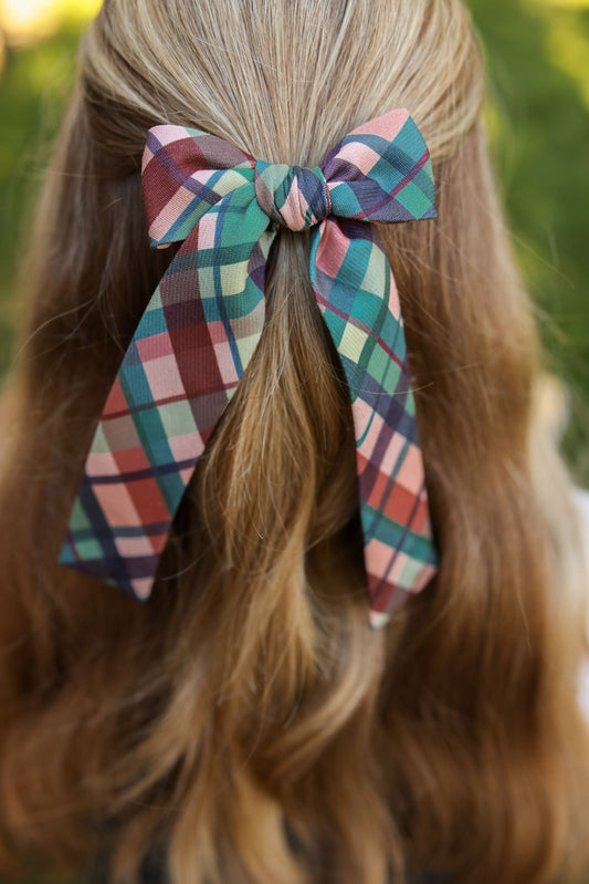 Plaid lady hair bow tied on blonde hair with long ribbon tails.