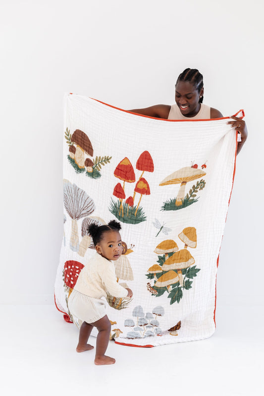 White throw blanket with colorful mushroom print and orange border, held folded over