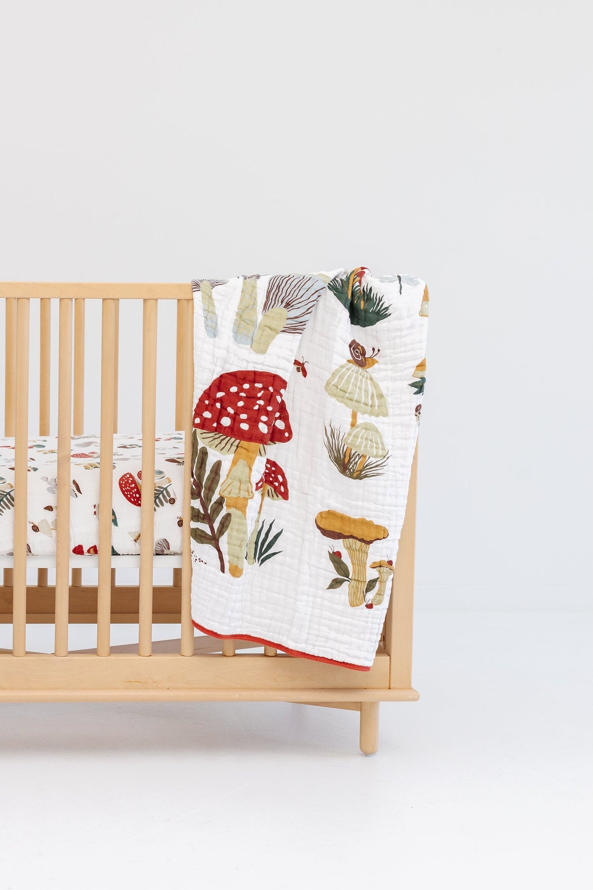 Children's quilt with white mushroom print and red scalloped border on crib