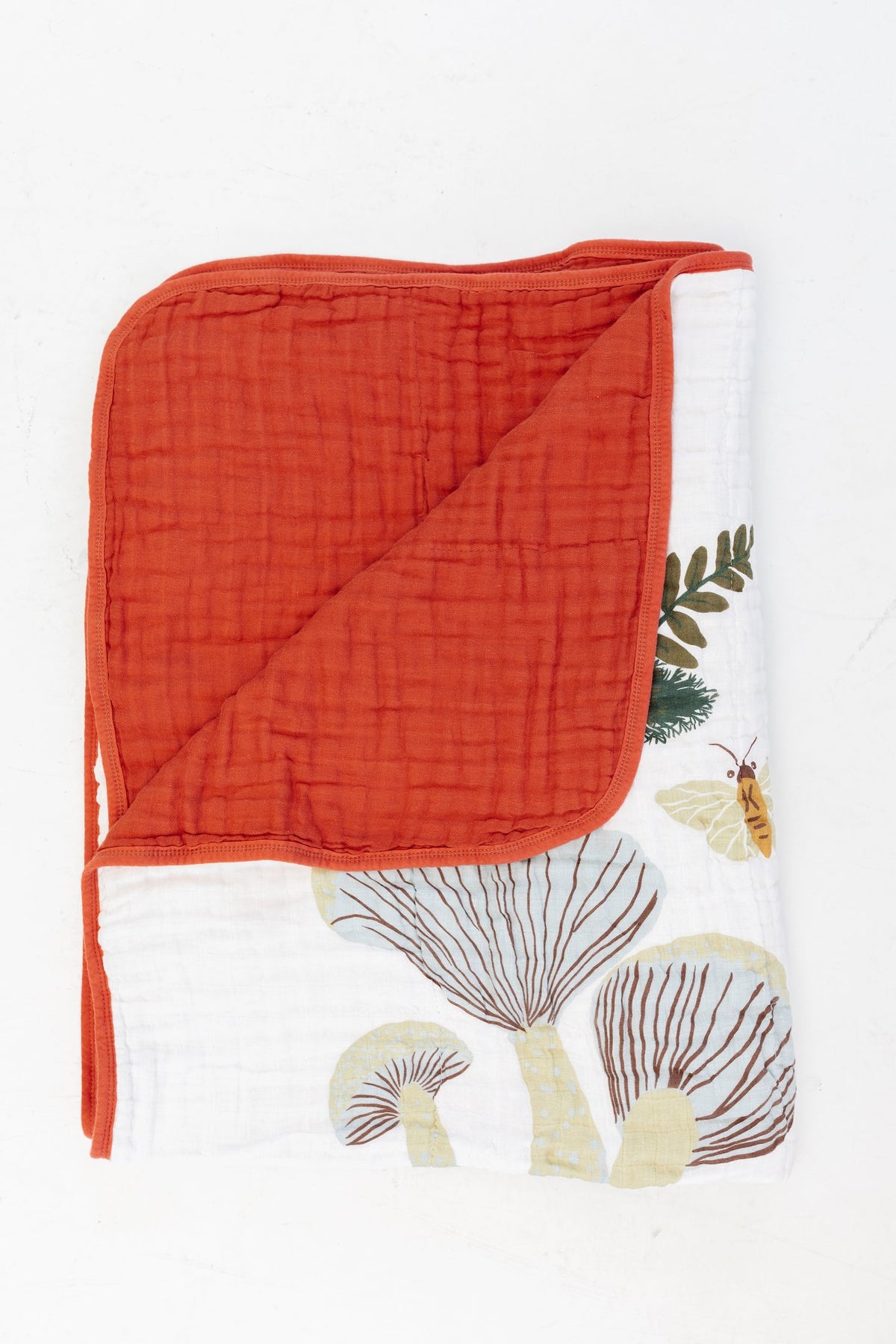 Folded throw blanket with orange quilted top and white fabric with mushroom print