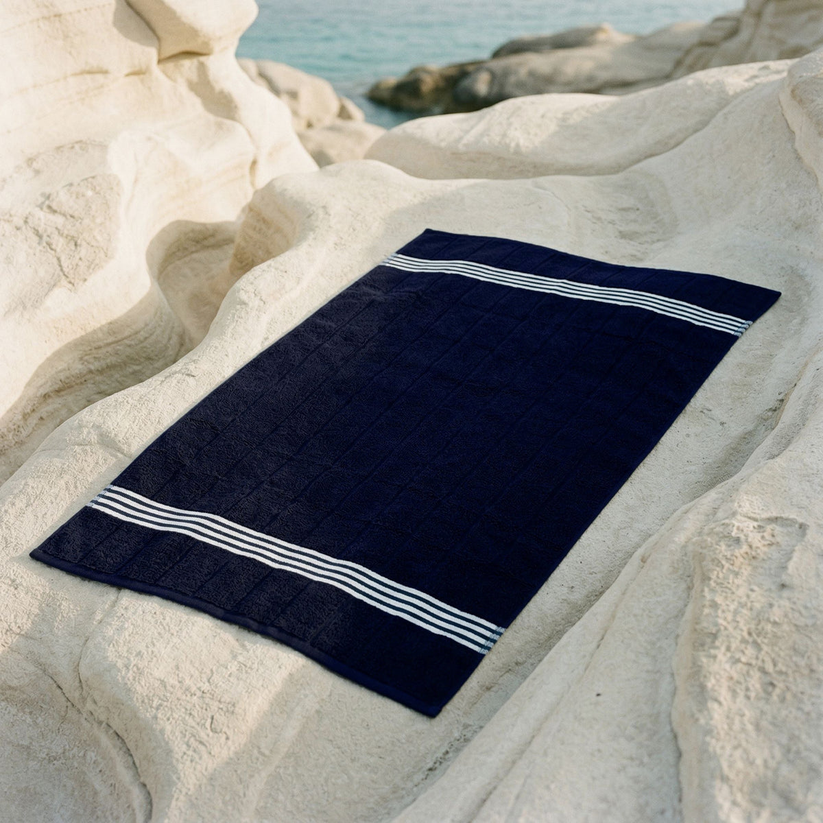 Nautilus Australian cotton towel, navy with white stripe borders on stone surface