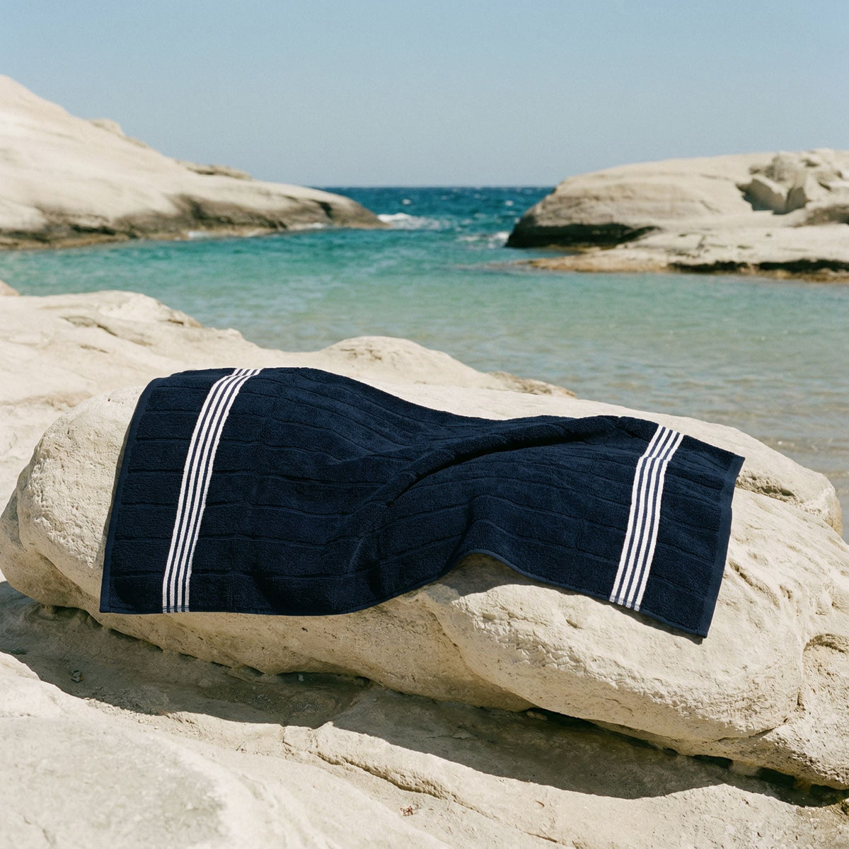Nautilus Australian cotton towel folded on rocks, navy with white stripe bands