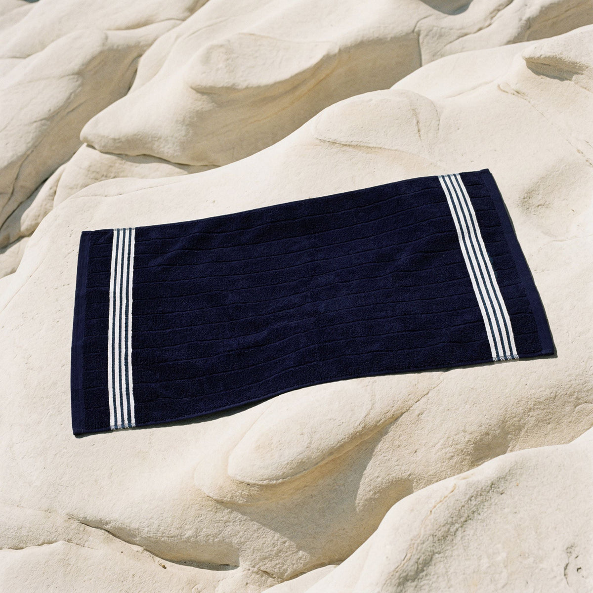Nautilus Australian cotton towel, navy rectangle with double white stripe borders on rocks