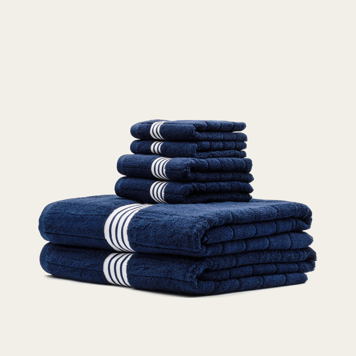Stack of navy towels with white triple-stripe bands and rolled edges