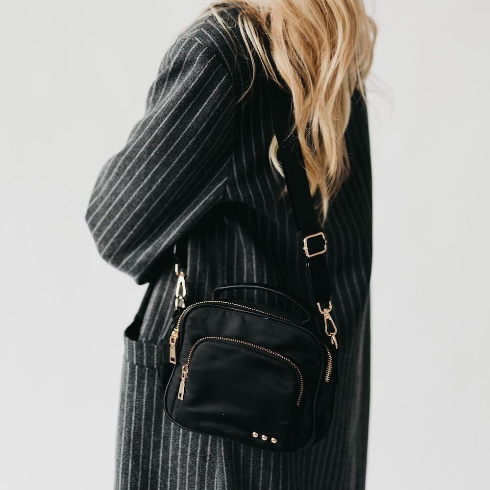 Black nylon crossbody bag on shoulder with front zip pocket and chain accents