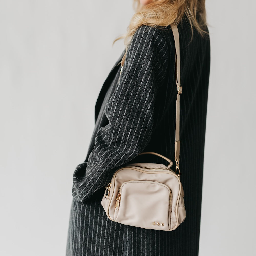 Taupe nylon crossbody bag on shoulder with small front zip pocket
