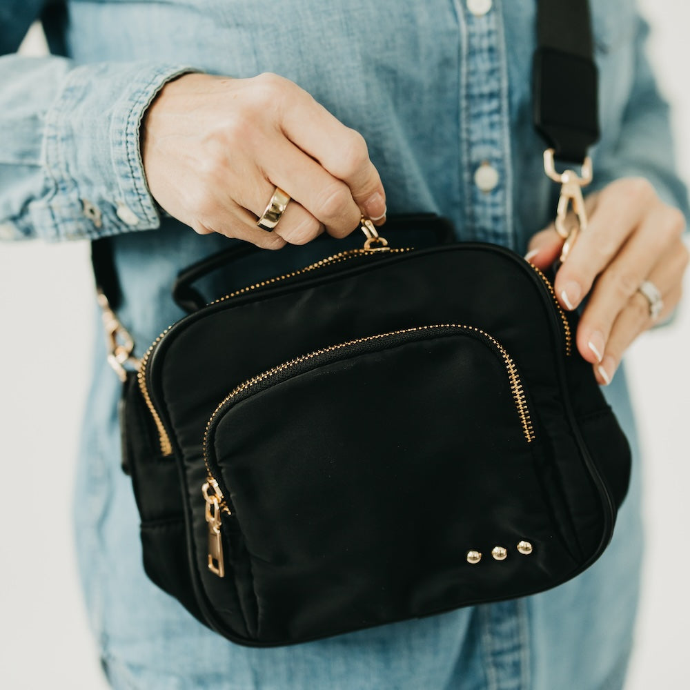 Black nylon crossbody bag close-up with curved front and gold-tone zipper pulls