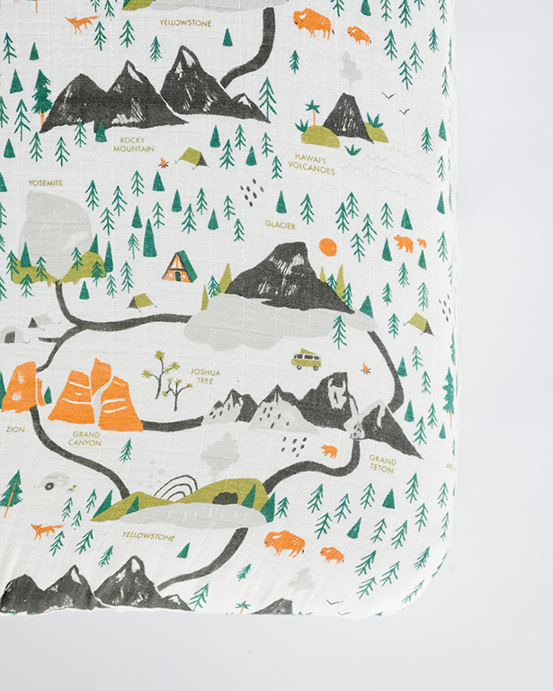 White crib sheet with national parks map print, mountains, trees, and animals in green and orange.