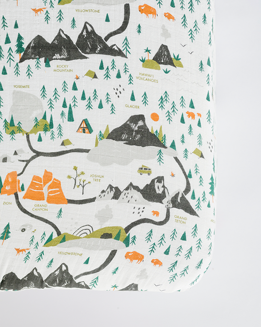 White crib sheet with national parks map print, mountains, trees, and animals in green and orange.