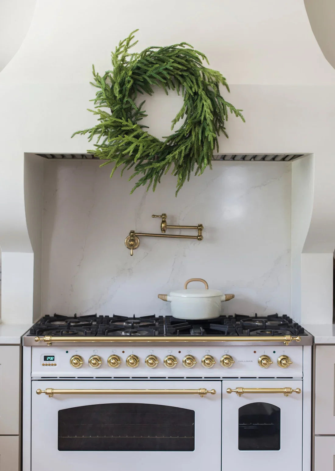 Green faux pine Christmas wreath mounted above a kitchen stove hood.