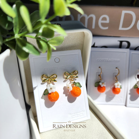 Orange fruit drop earrings with white flower, green leaf accents, gold bow-tie studs