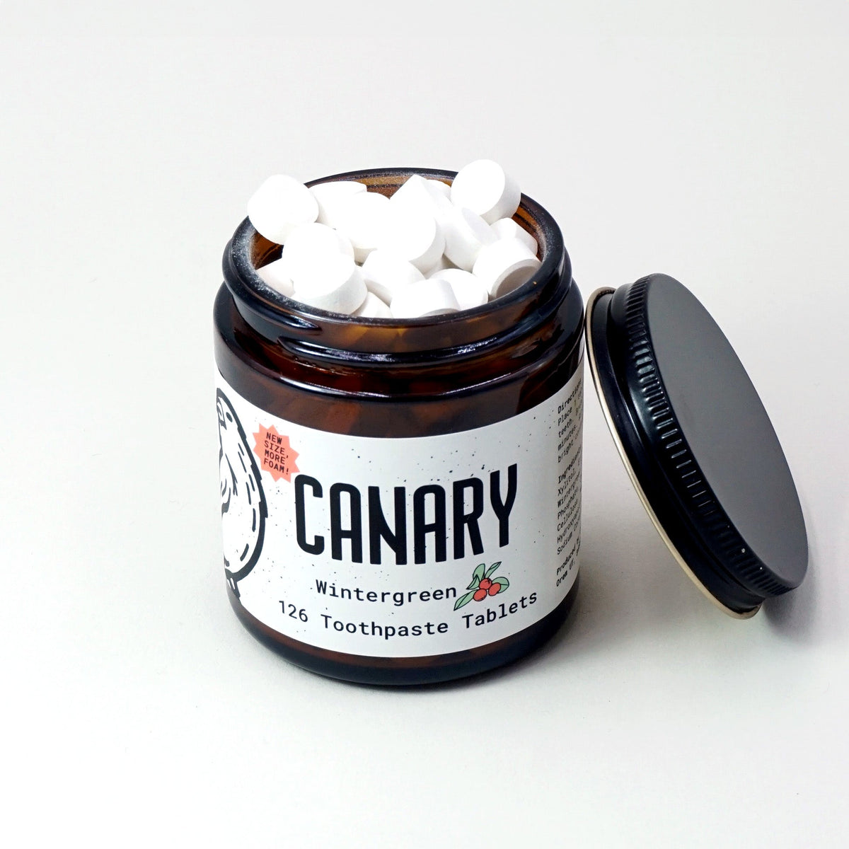 Open jar of white toothpaste tablets with its black lid beside it