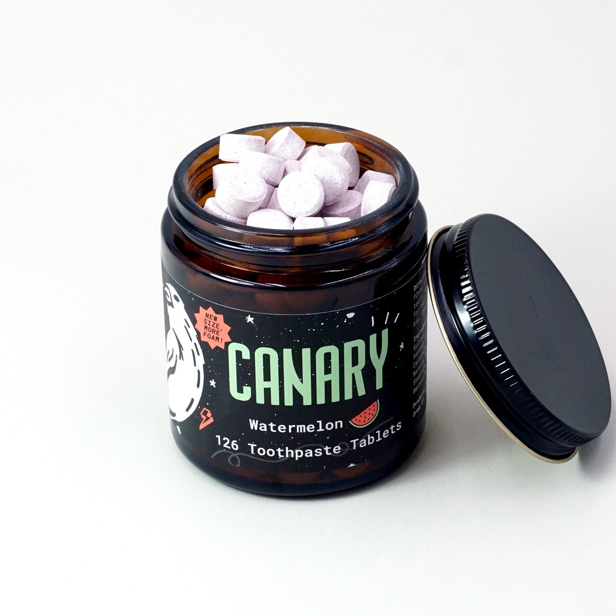 Open jar of watermelon toothpaste tablets with its black lid beside it.