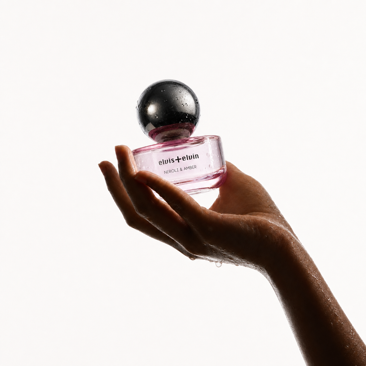 Perfume bottle with pink glass and black dome cap held in hand