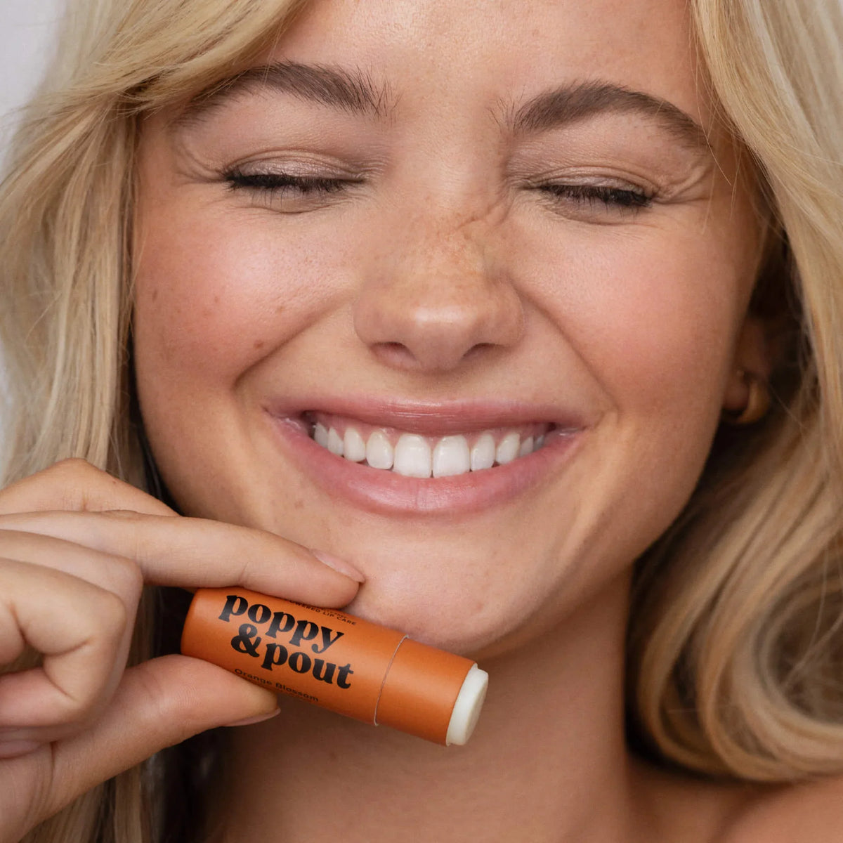 Orange blossom lip balm tube held by smiling person near lips