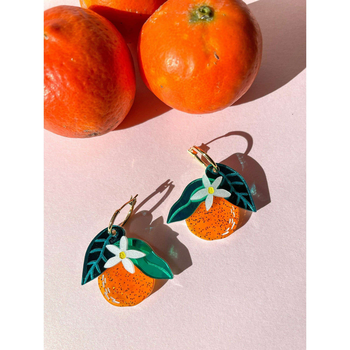 Orange dangle earrings with orange fruit charms, green leaves, white flowers, gold hooks