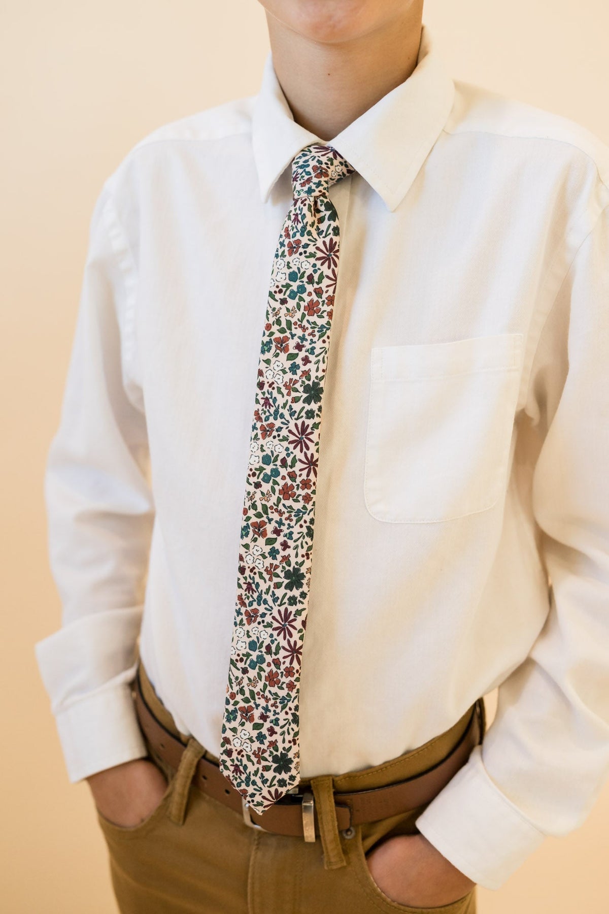 Floral youth necktie in cream with multicolor botanicals, worn with a white button-down