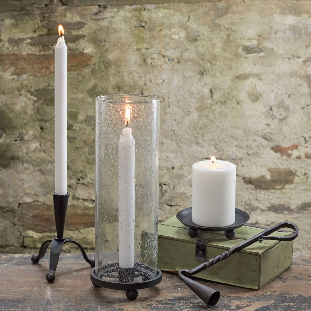 Wrought iron candle snuffer on tabletop beside lit pillar candles and glass holder