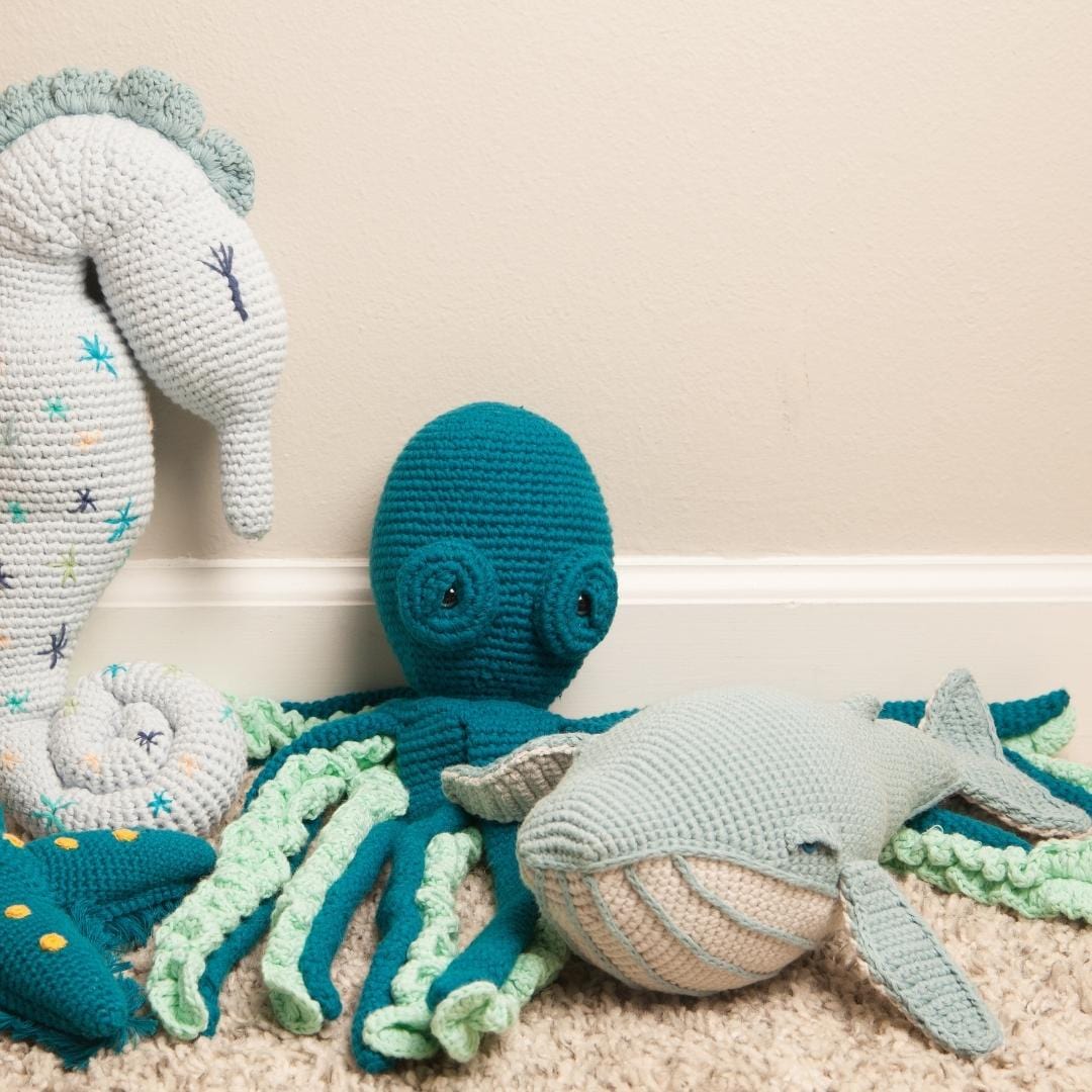 Misty blue crocheted whale plush with a cream striped belly and outstretched fins.
