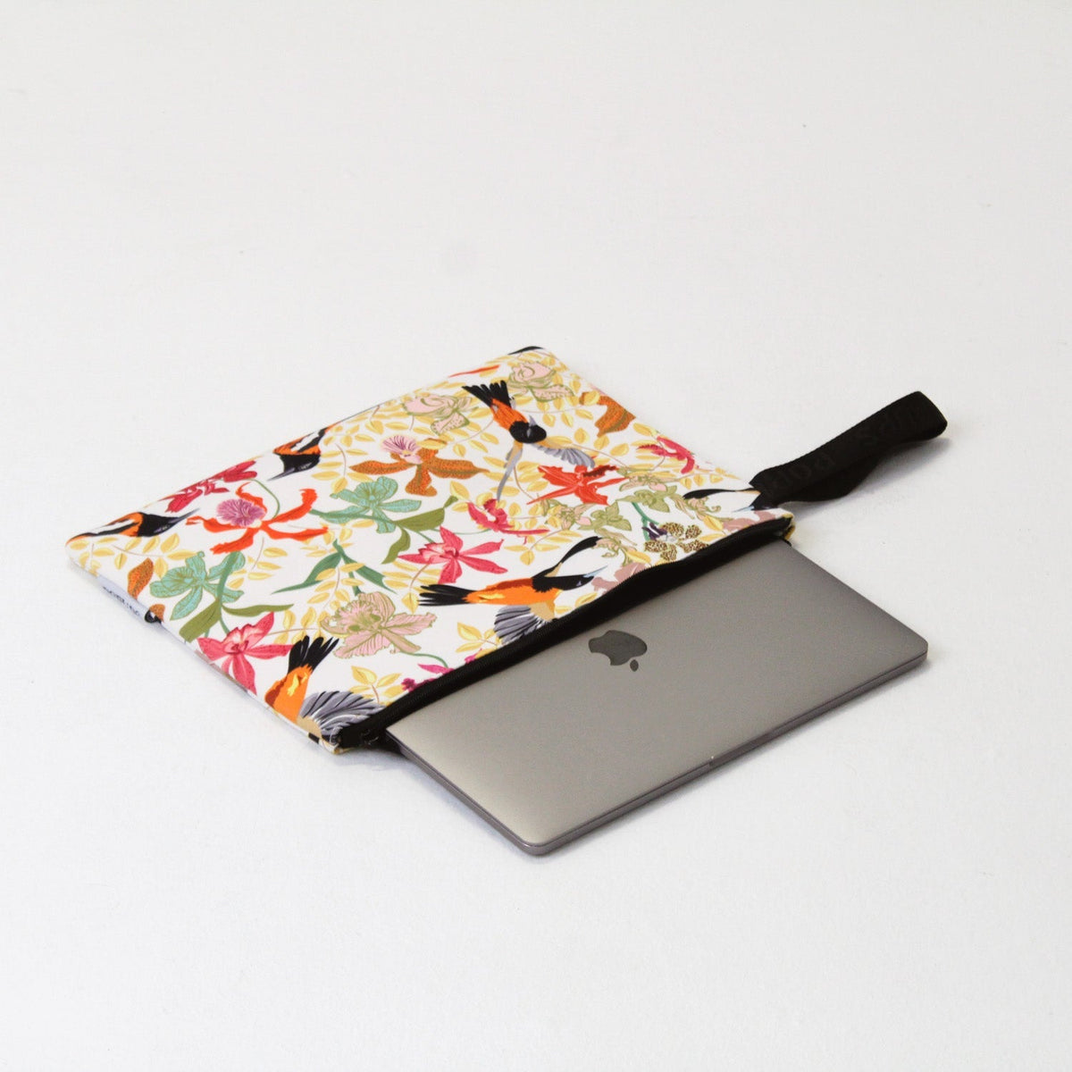Tropical laptop sleeve with black trim holding a slim gray laptop, zipper edge