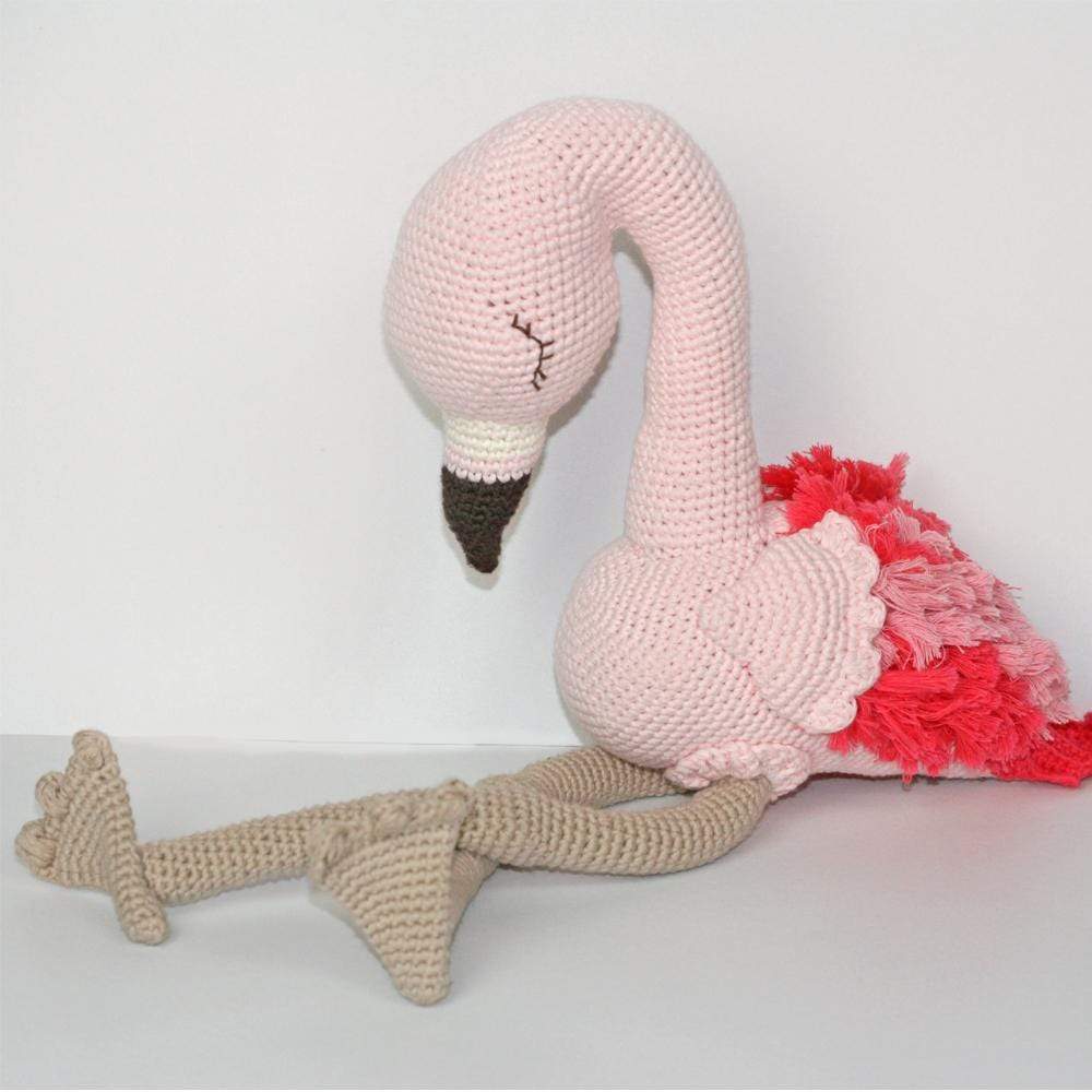 Crocheted flamingo plush sitting with its long tan legs extended