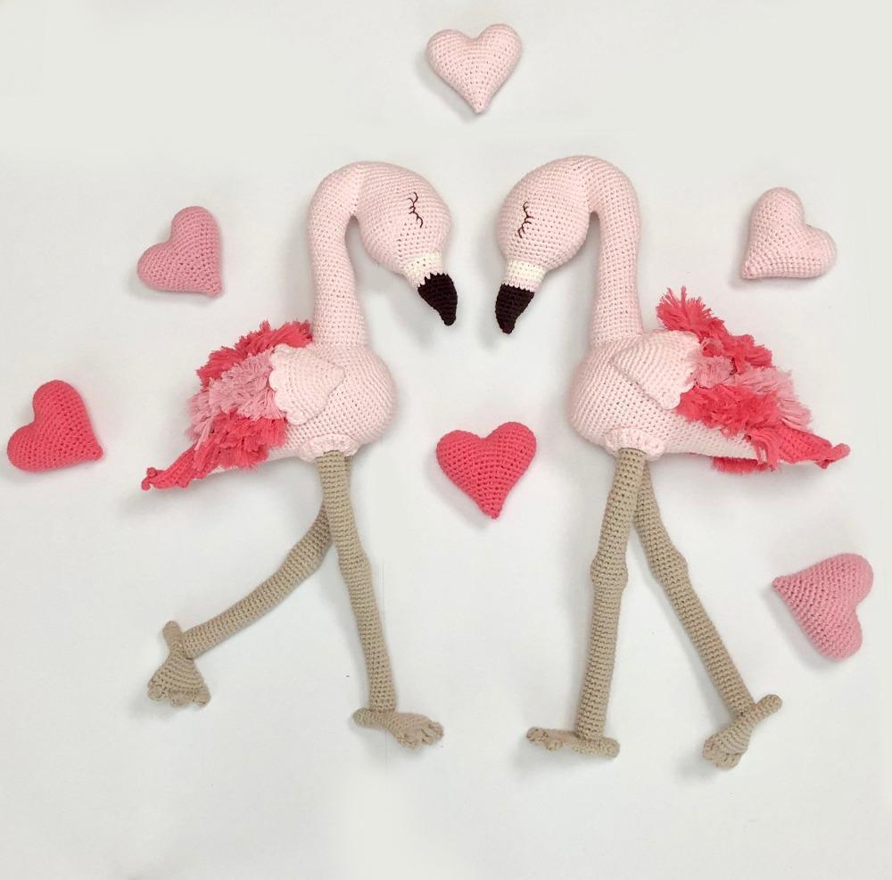 Two crocheted pink flamingo plush toys with bright pink feathered wings and long tan legs