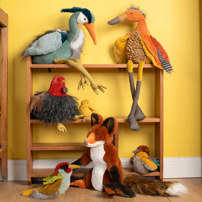 Brown plush fox doll sitting on the floor among other stuffed animals.