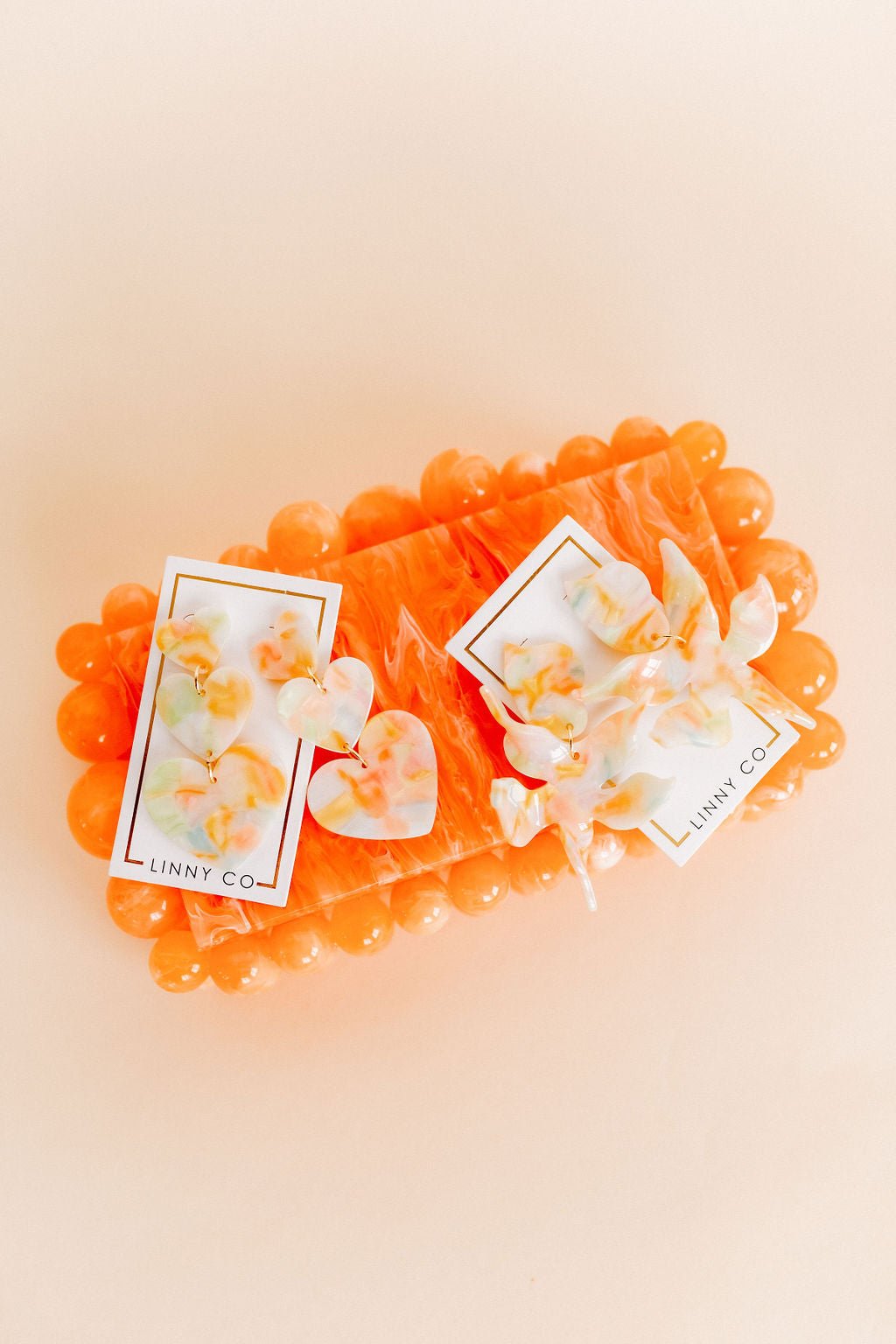 Layered heart-drop earrings with orange and white iridescent hearts, gold hooks