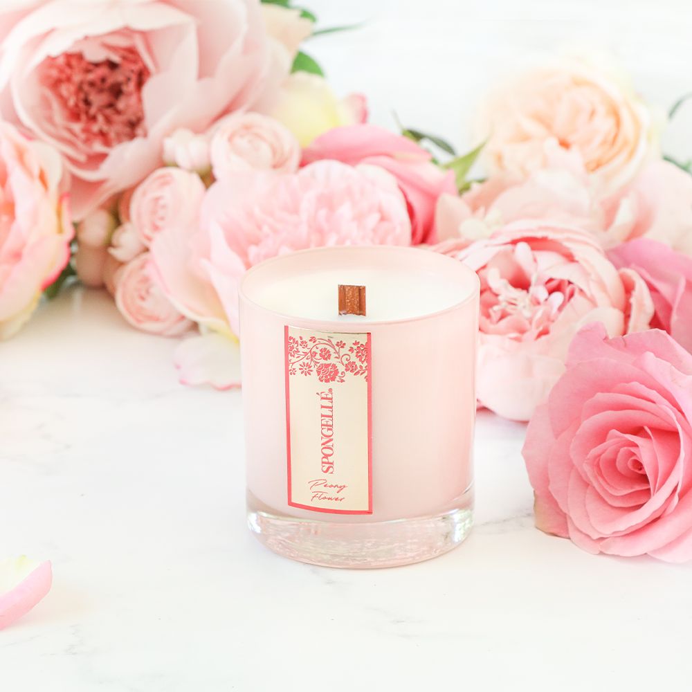 Pink glass scented candle with floral label, with pink roses nearby