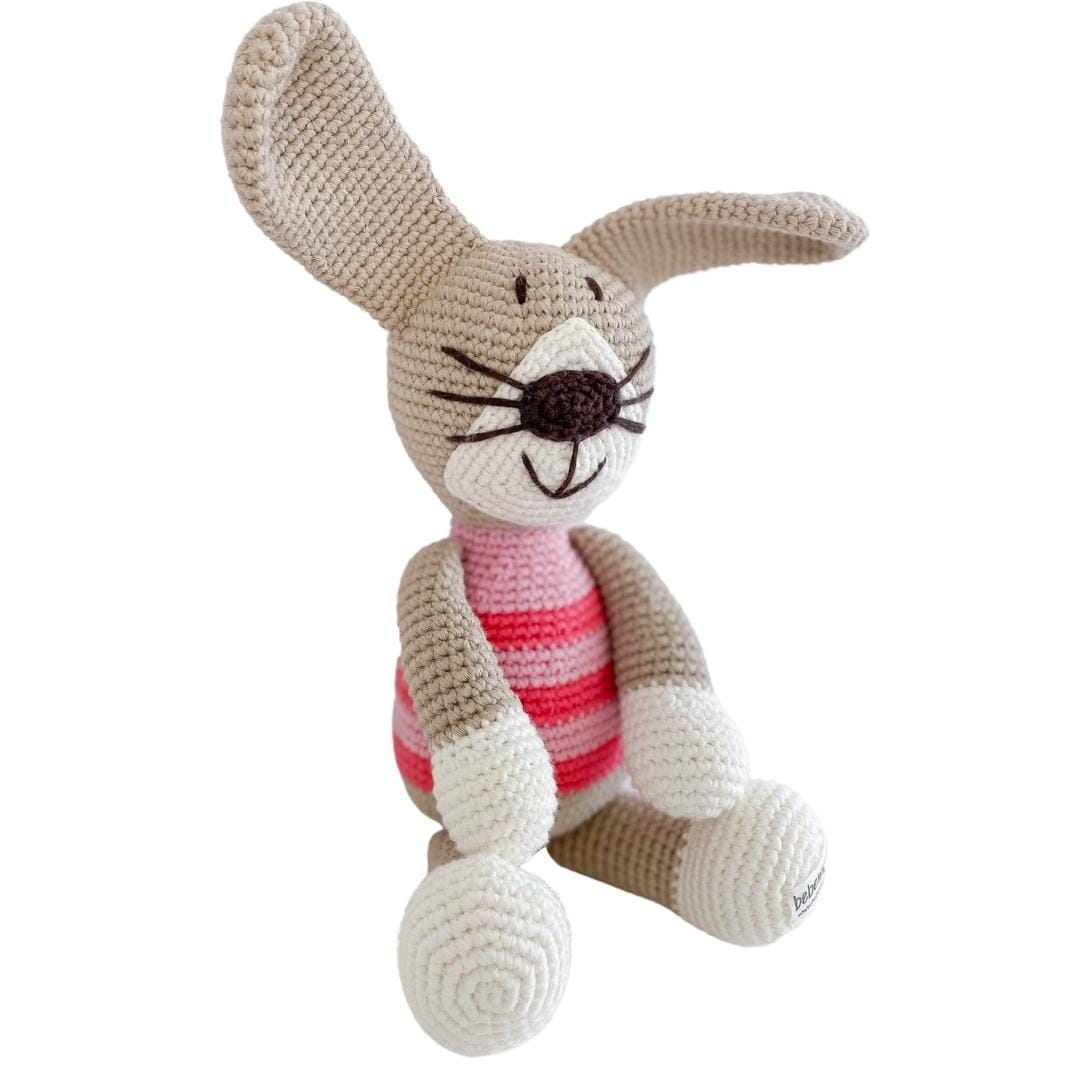 Seated crocheted rabbit plush with beige fur, white feet, and pink stripes