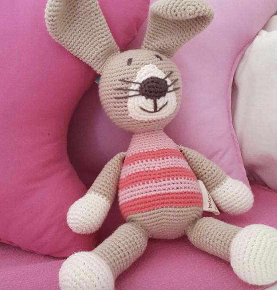 Crocheted rabbit toy with long ears, white paws, and a pink striped body
