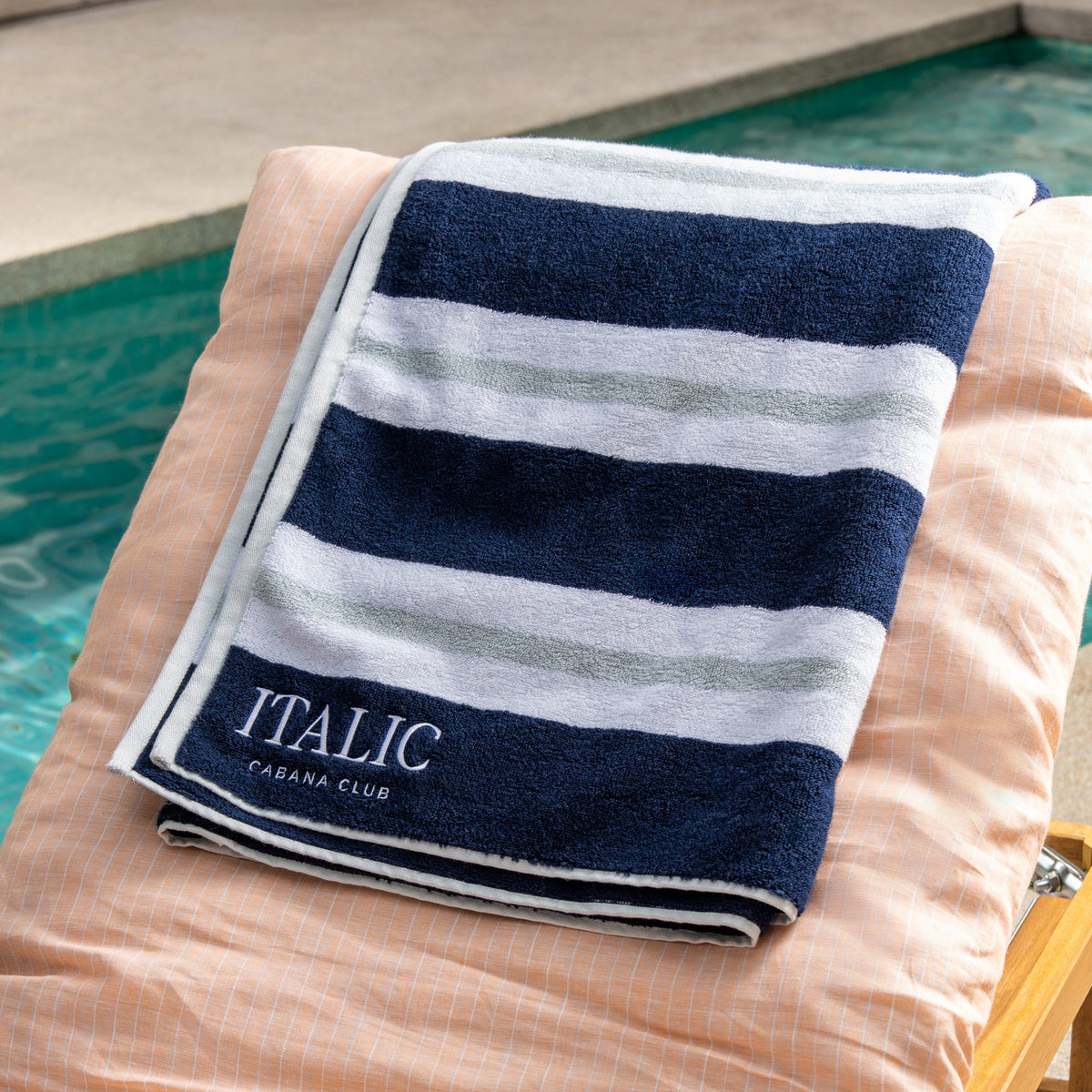 Navy and white striped cotton beach towel with logo label, folded on lounge