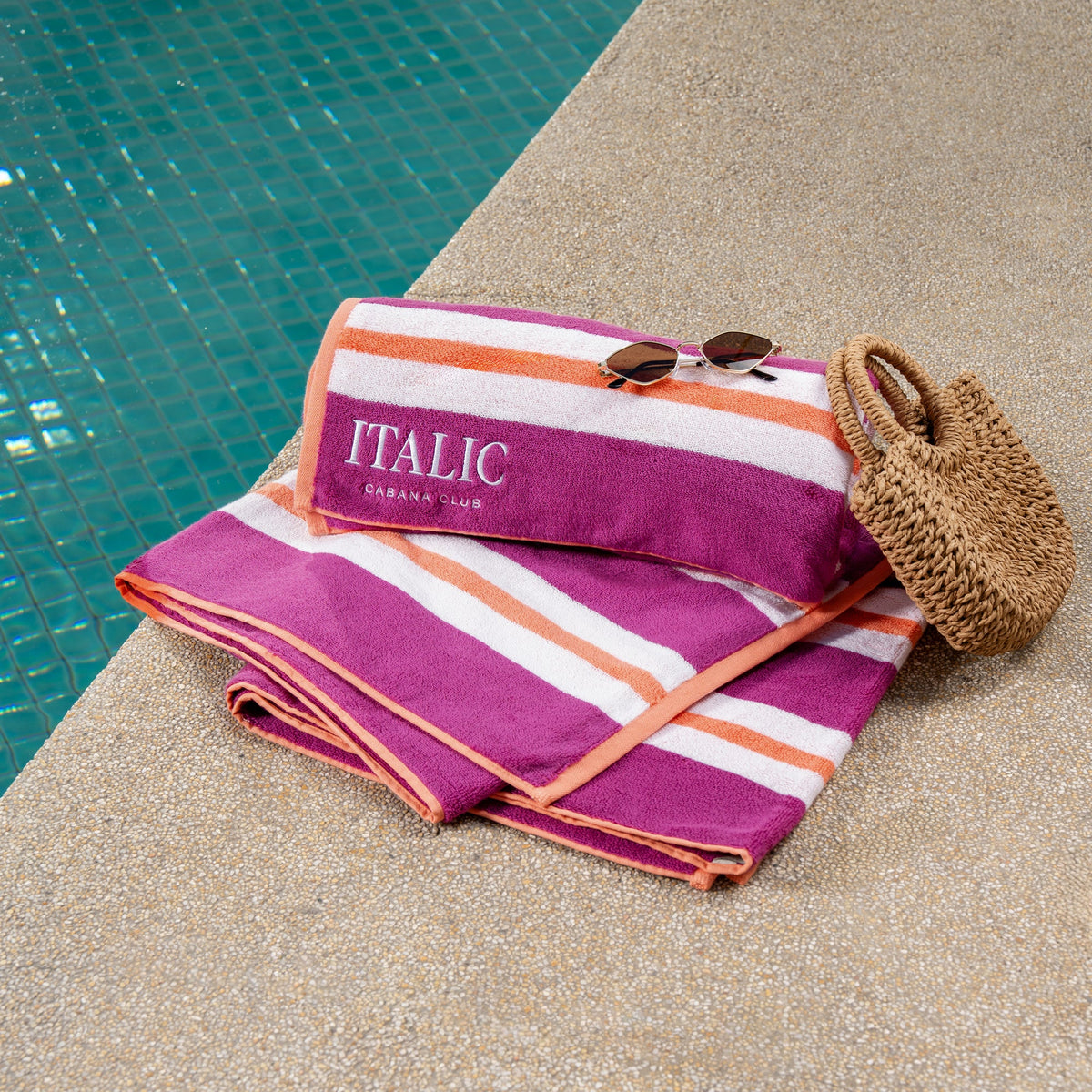 Pink and white striped cotton beach towel with orange stripe detail, folded on deck