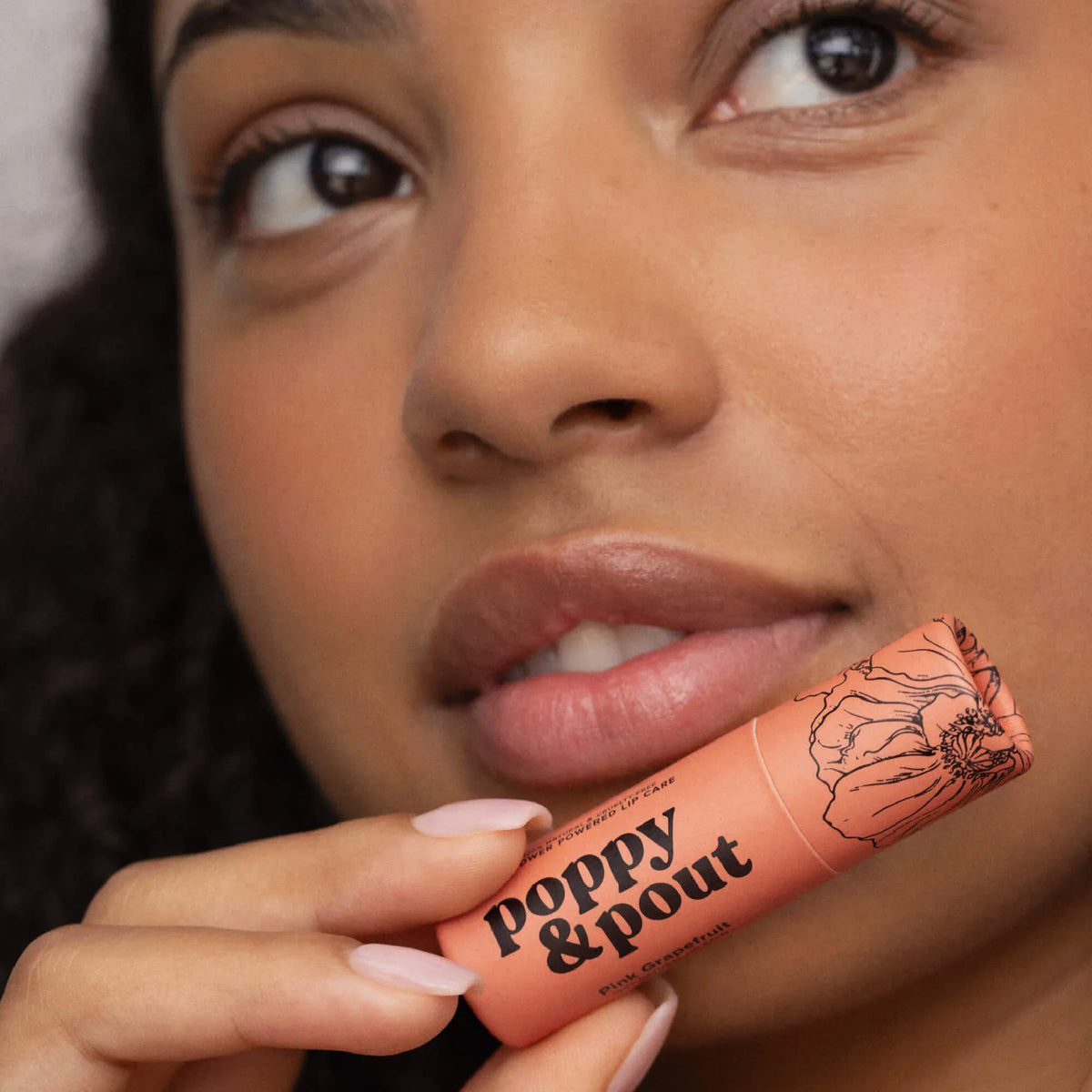 Pink grapefruit lip balm tube near lips with hand holding it