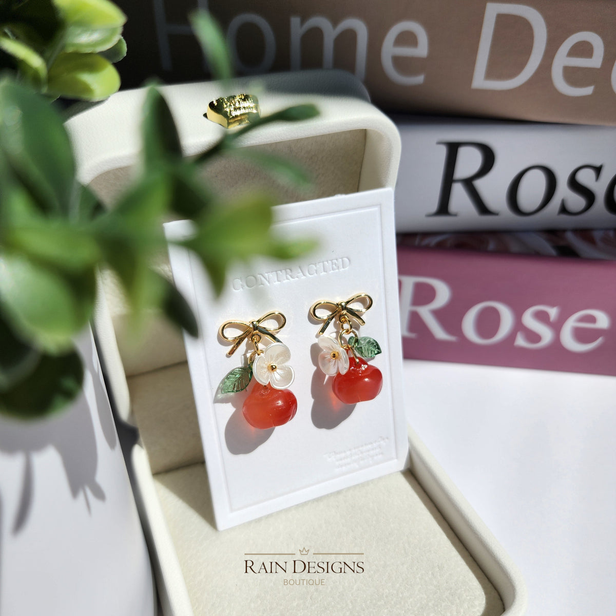 Gold apple earrings on card: red fruit charms with white flowers and green leaves