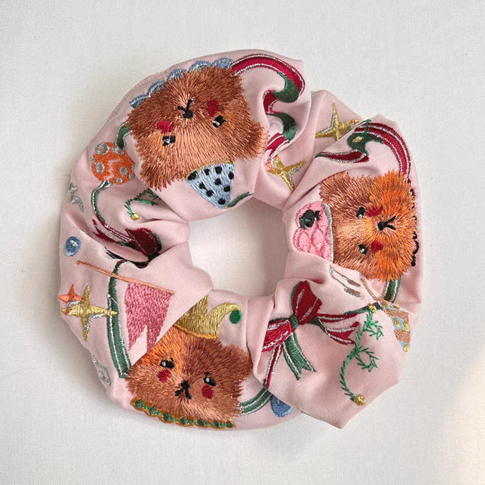 Pink scrunchie with embroidered circus bear faces and star-and-ribbon motifs