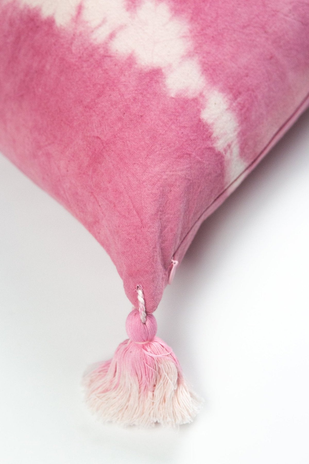 Pink shibori tie-dye pillow with white pattern and round tassel at the bottom corner.