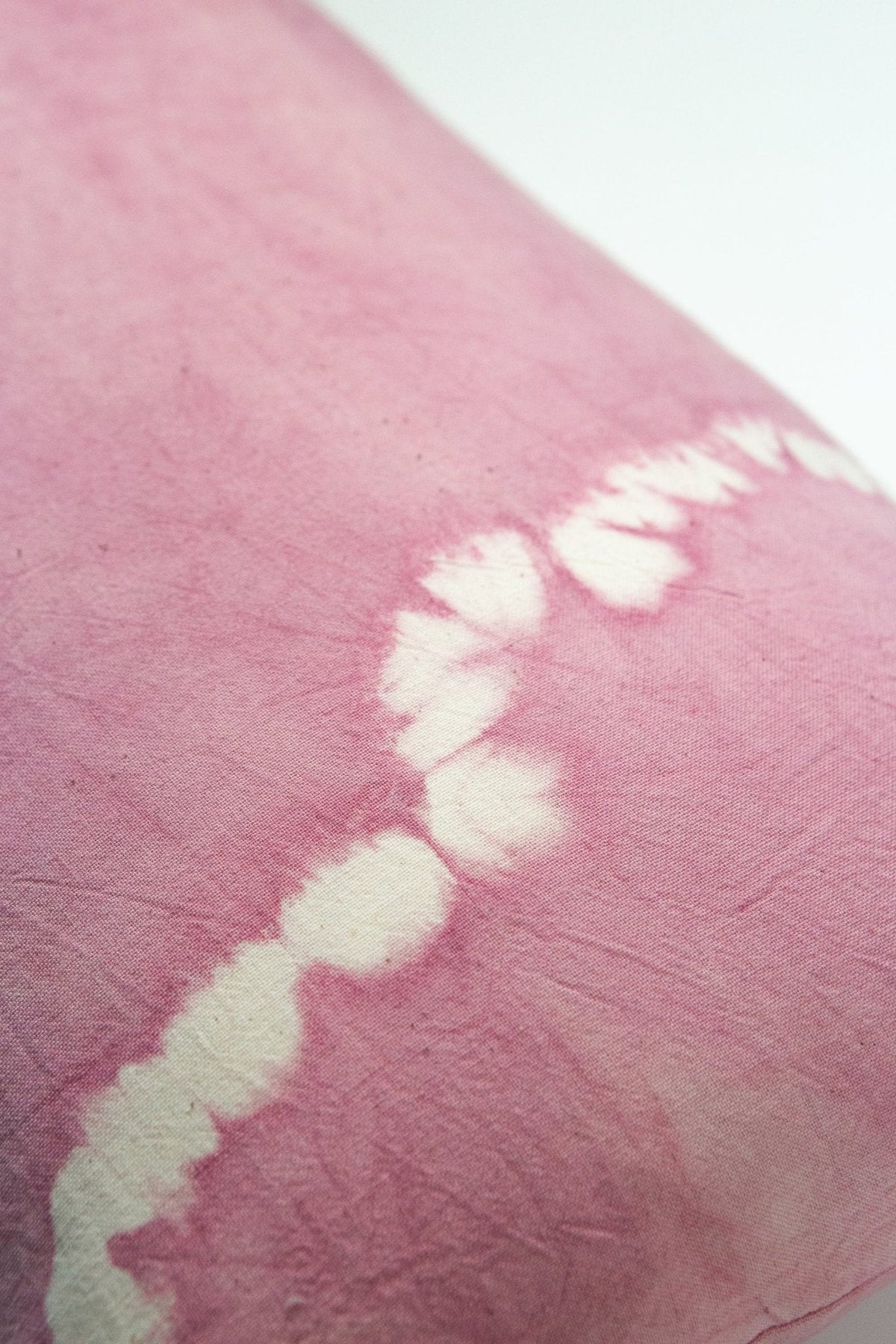 Close-up of pink shibori tie-dye fabric with white knot pattern and soft textured surface.