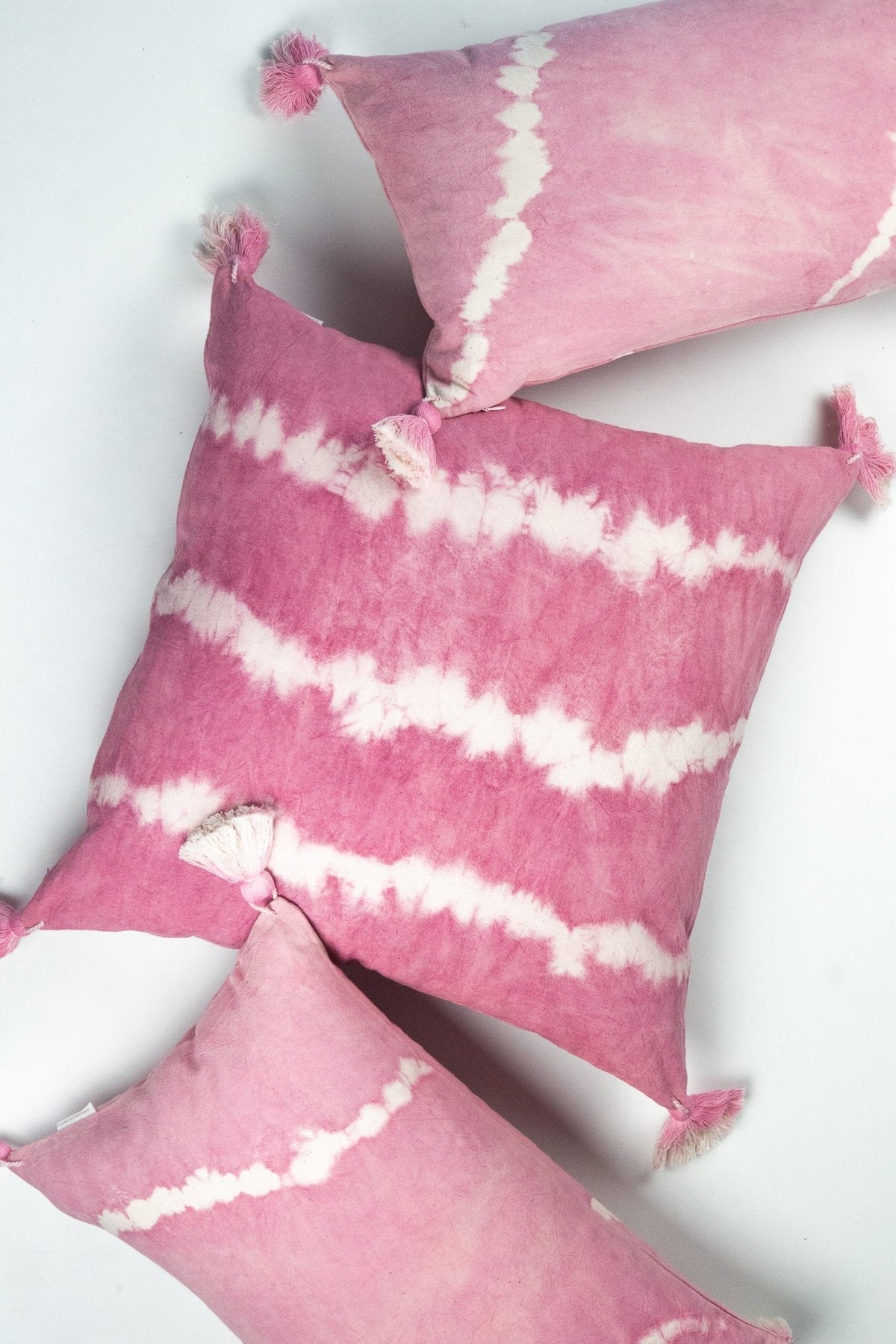 Pink shibori tie-dye tassel throw pillow with white swirl pattern and fringe corners.