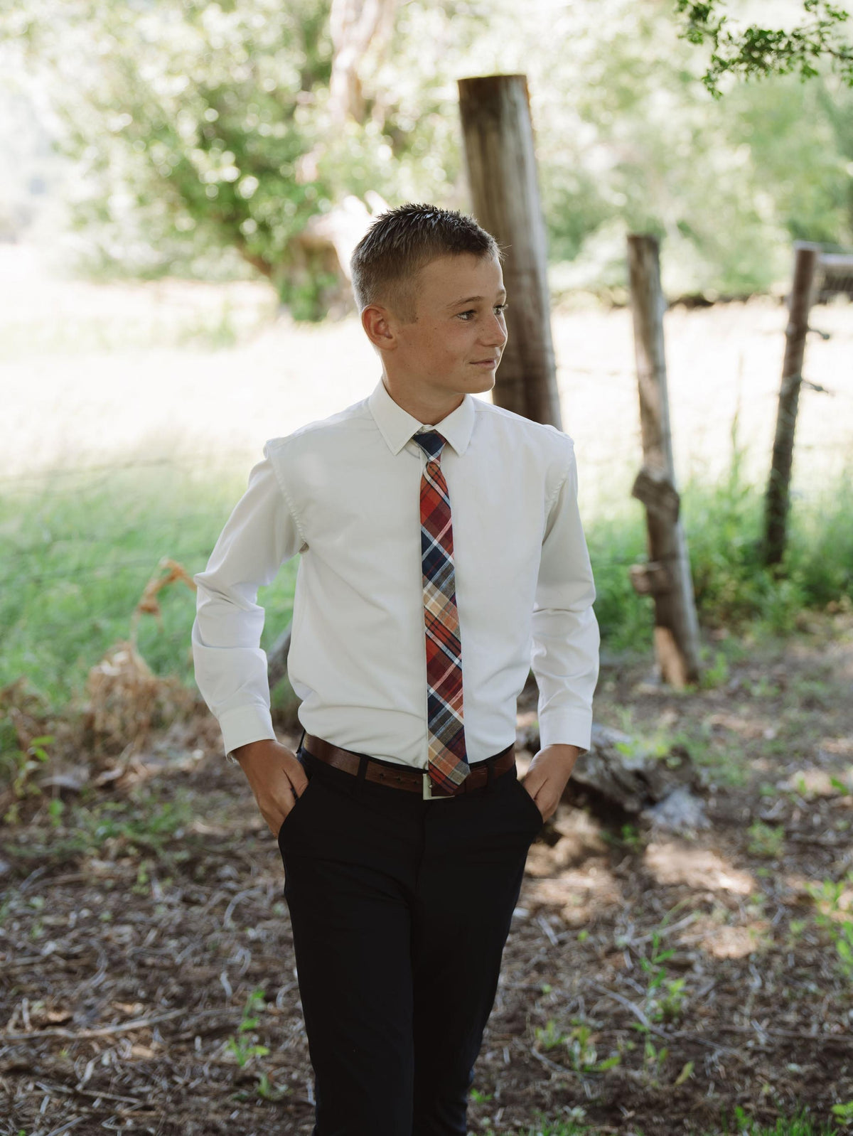 Boys plaid necktie worn with a white button-down shirt and brown belt.