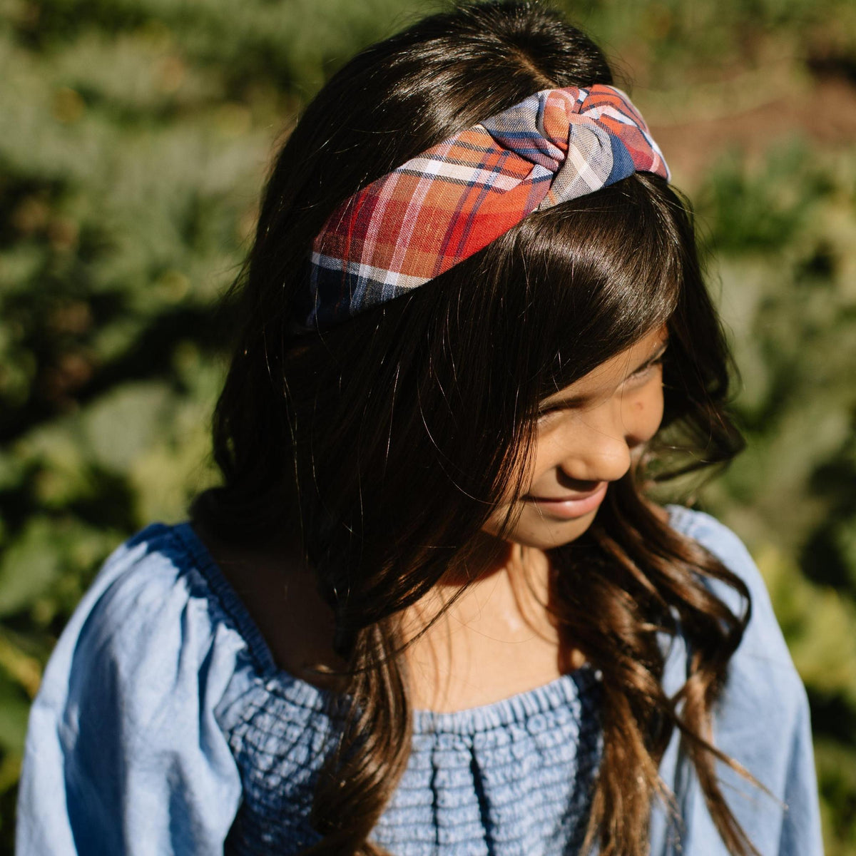 Plaid knotted headband worn on dark hair, orange blue red and white checks