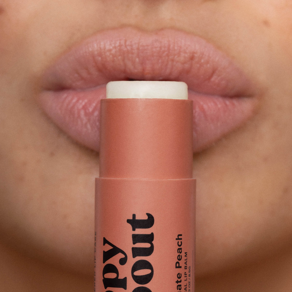 Pomegranate peach lip balm stick tube close-up against lips