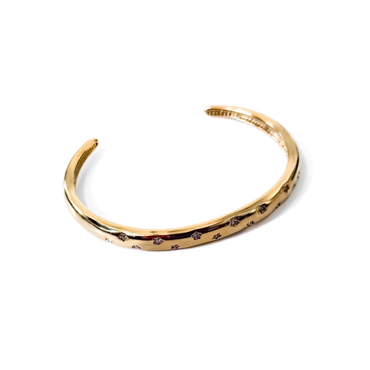 Gold-tone open cuff bangle with rhinestone border, flat lay