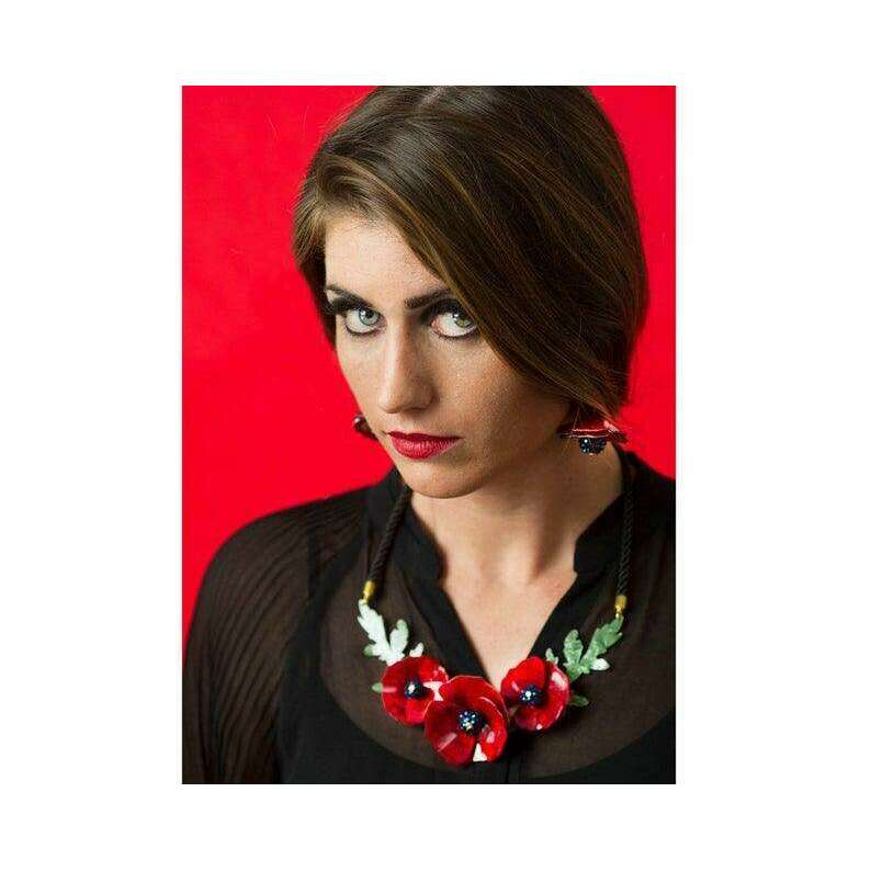 Red poppy necklace with green leaves worn on a woman’s neckline, black top